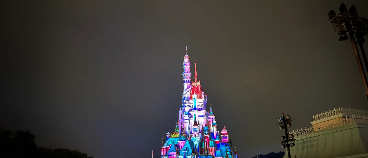 Hong Kong Disneyland's castle lit with a projection-mapped night show, seen from a crowded Main Street
