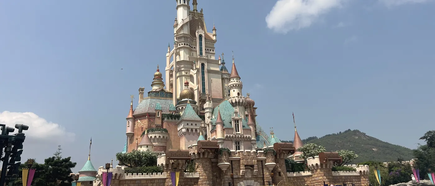 Hong Kong Disneyland's castle seen from below, with the green hills of rural Lantau Island rising behind it