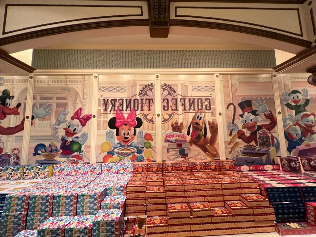 A confectionery and gift shop at Tokyo Disneyland, shelves stacked with boxed treats beneath a mural of classic Disney characters