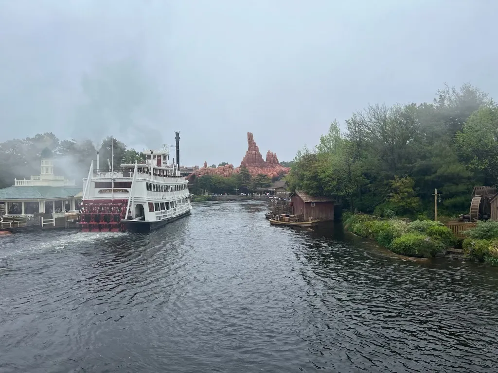 A steamboat and quiet river at Tokyo Disneyland on a misty morning, with Big Thunder Mountain visible in the distance