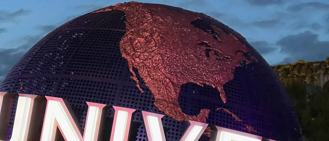 The Universal Studios Japan entrance globe lit up at dusk, with the neon Universal lettering beneath it
