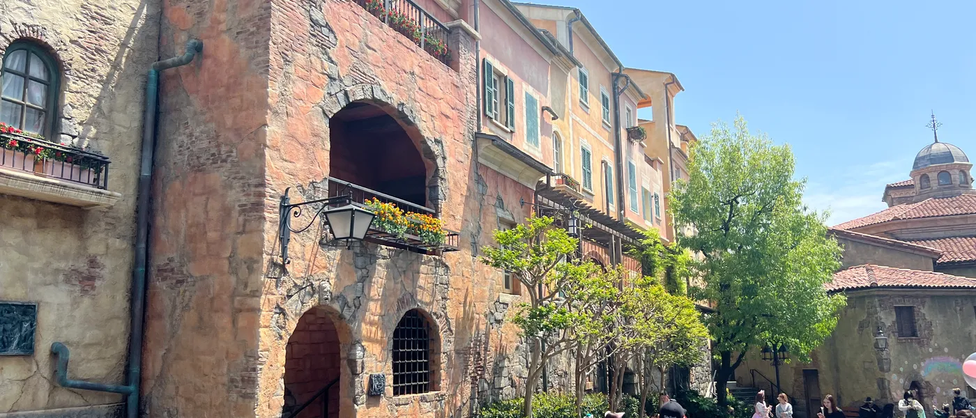 A sunlit Mediterranean-style street at Tokyo DisneySea, with warm stone buildings and visitors walking beneath the balconies